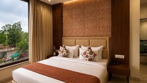 A hotel room with a large bed, a ceiling fan, a nightstand, and a view of the outdoors. - Regenta Place Kota (Kota)