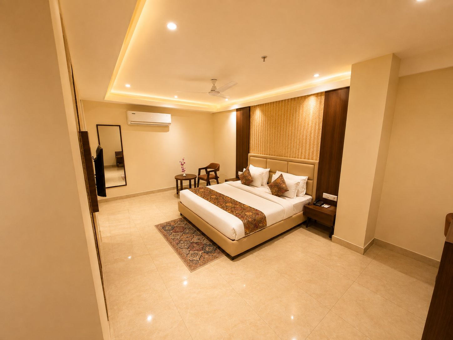 A modern hotel room with a large bed, bedside tables, a small seating area, and a ceiling fan.