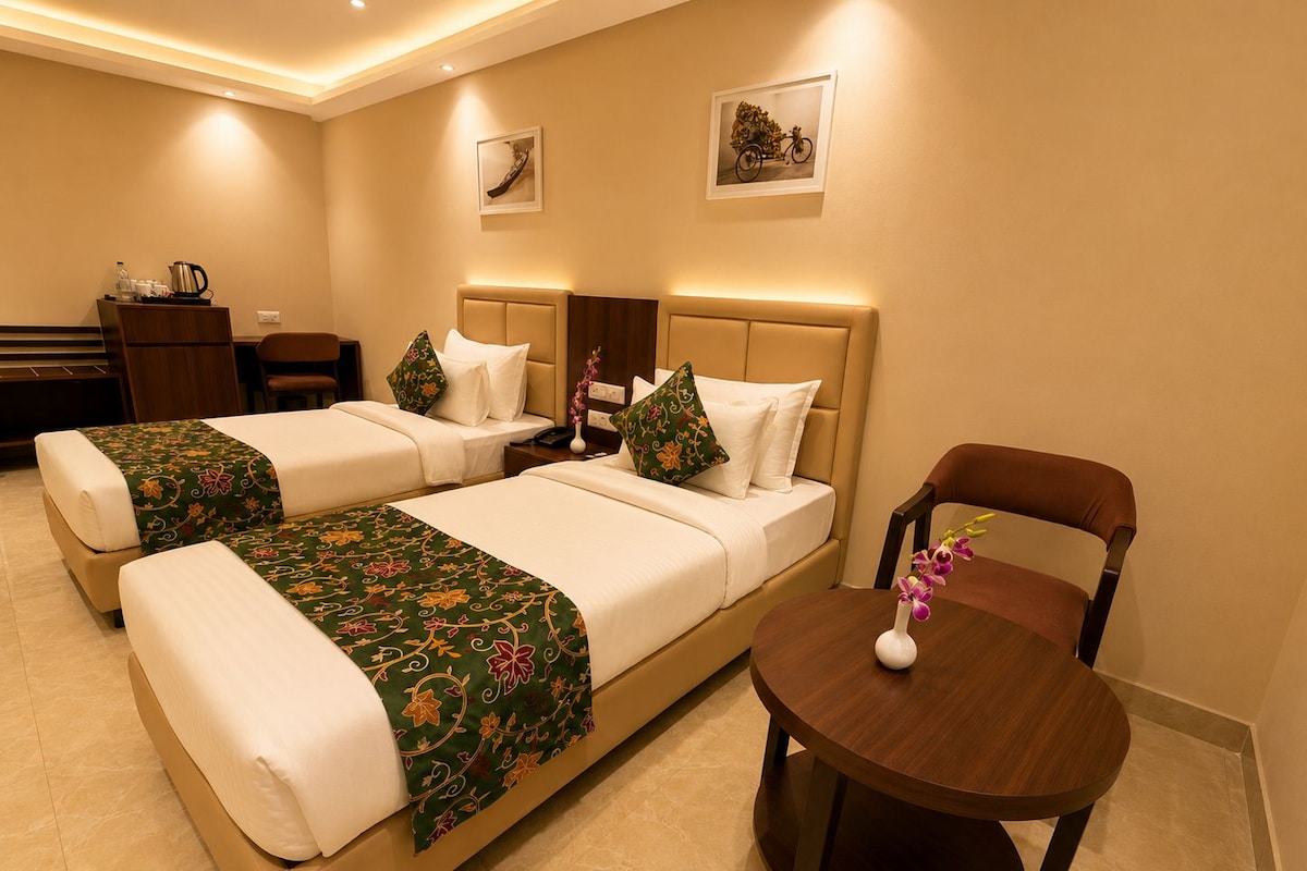 Habitación de hotel con dos camas, una mesita pequeña y una silla.