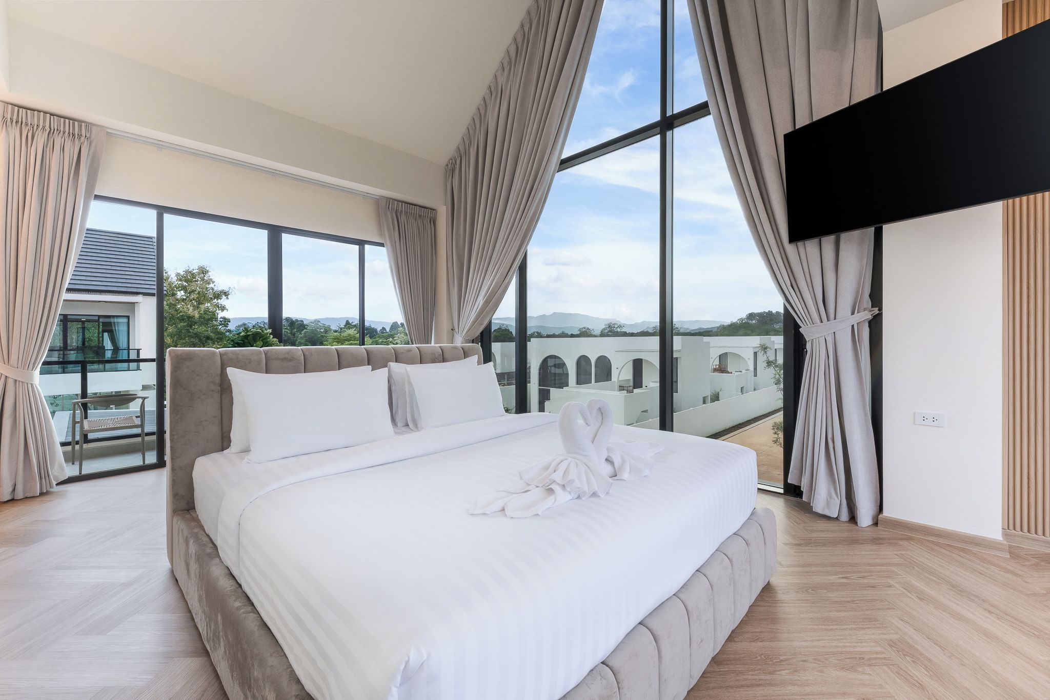 Un dormitorio moderno con una cama grande, un televisor de pantalla plana y vistas a un edificio y un paisaje.