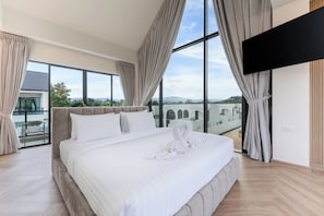 Un dormitorio moderno con una cama grande, un televisor de pantalla plana y vistas a un edificio y un paisaje.
