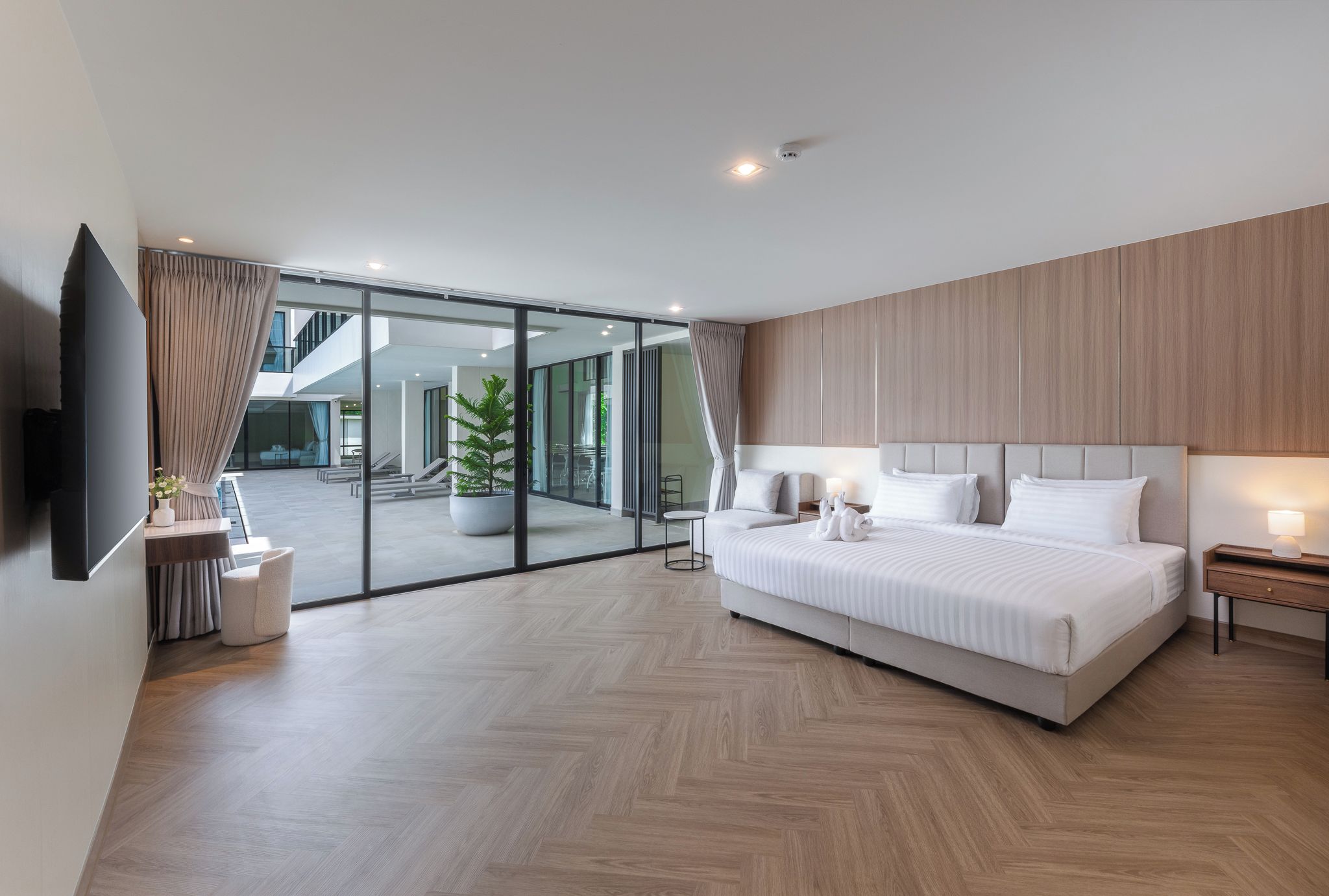 Un dormitorio moderno con una cama grande, un televisor montado en la pared y un ventanal corredero que da a un espacio exterior.