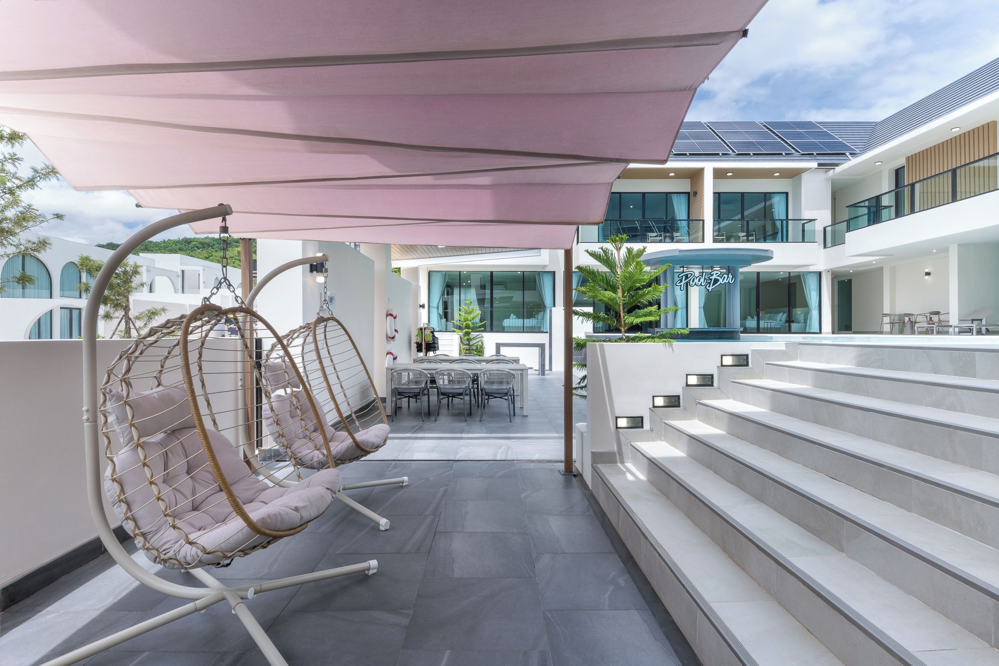 A modern outdoor seating area with a pool bar, a dining area, and a staircase leading to an upper level.