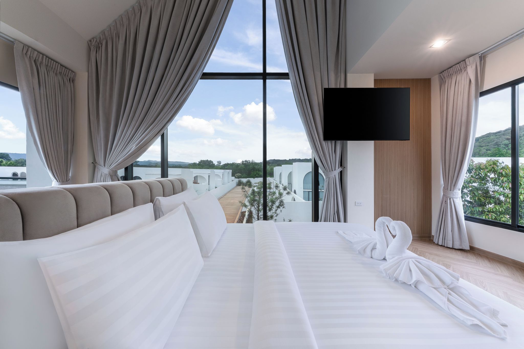 A modern hotel room with a large bed, a flat-screen TV, and a view of a coastal landscape.
