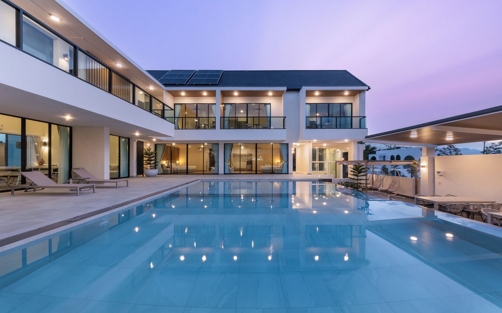 A modern two-story house with a swimming pool, large windows, and solar panels.