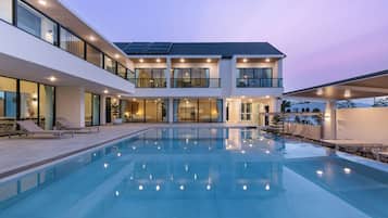 A modern two-story house with a swimming pool, large windows, and solar panels.