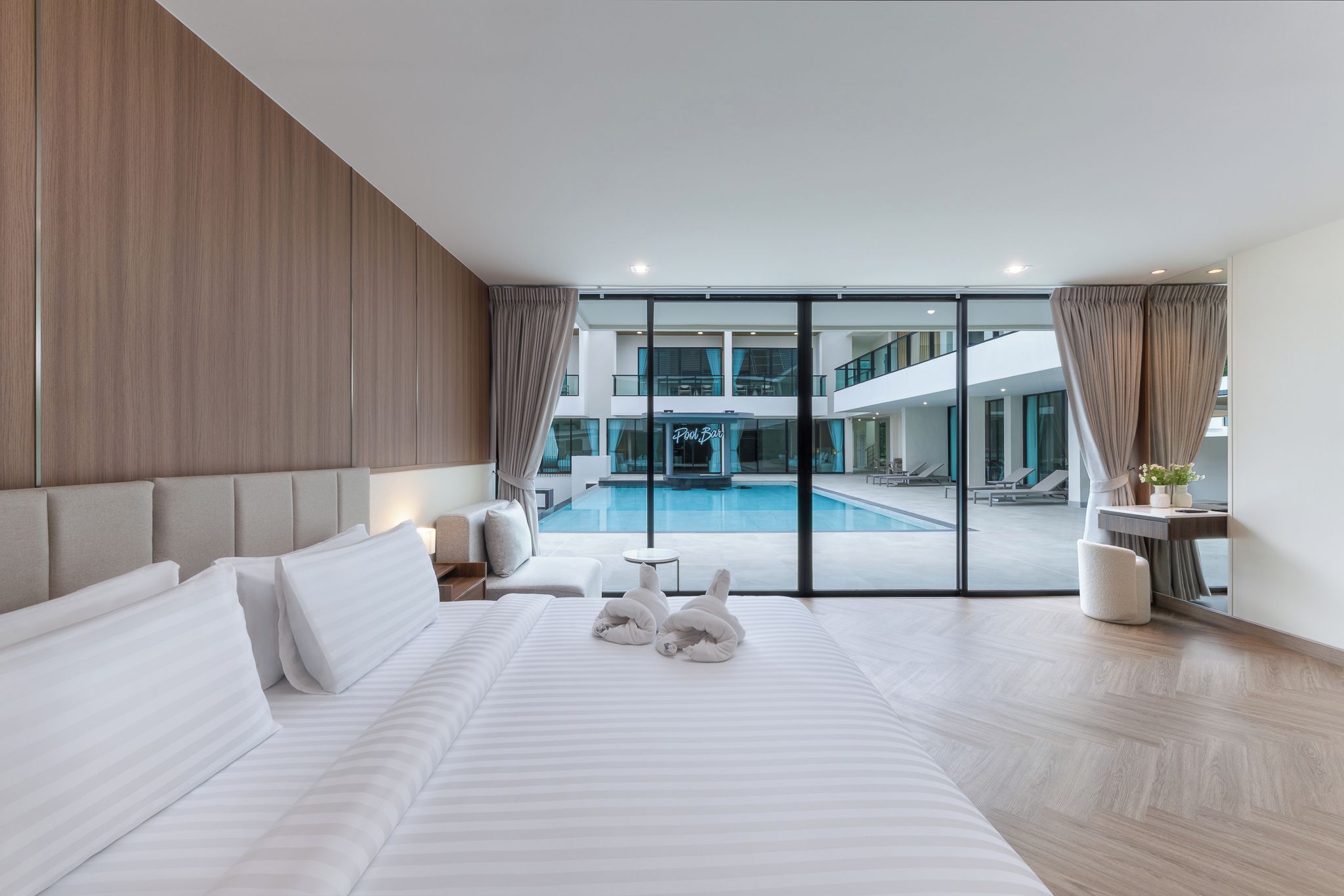 Habitación de hotel moderna con una cama grande, vistas a una zona de piscina y un balcón.