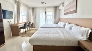 Ein Hotelzimmer mit einem großen Bett, einem Schreibtisch mit Stuhl, einem Fernseher und einem Fenster mit Vorhängen.