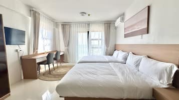 Quarto de hotel com uma cama grande, uma escrivaninha com cadeira, televisão e janela com cortinas.