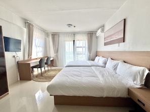 Quarto de hotel com uma cama grande, uma escrivaninha com cadeira, televisão e janela com cortinas.