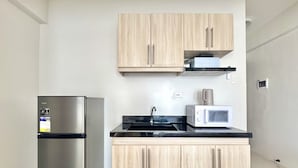 Eine kompakte Küche mit Edelstahlkühlschrank, Mikrowelle und Holzschränken.