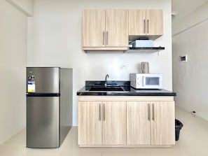 Cozinha compacta com geladeira de aço inoxidável, micro-ondas e armários de madeira.