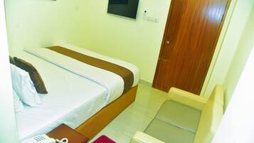 A hotel room with a bed, a bedside telephone, a small table, a television on the wall, and a wooden door.