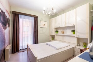 A bedroom with a bed, a nightstand, a dresser, a chandelier, and a window with curtains. - Apartment in Blankenberge Near Belgium Pier (Blankenberge)