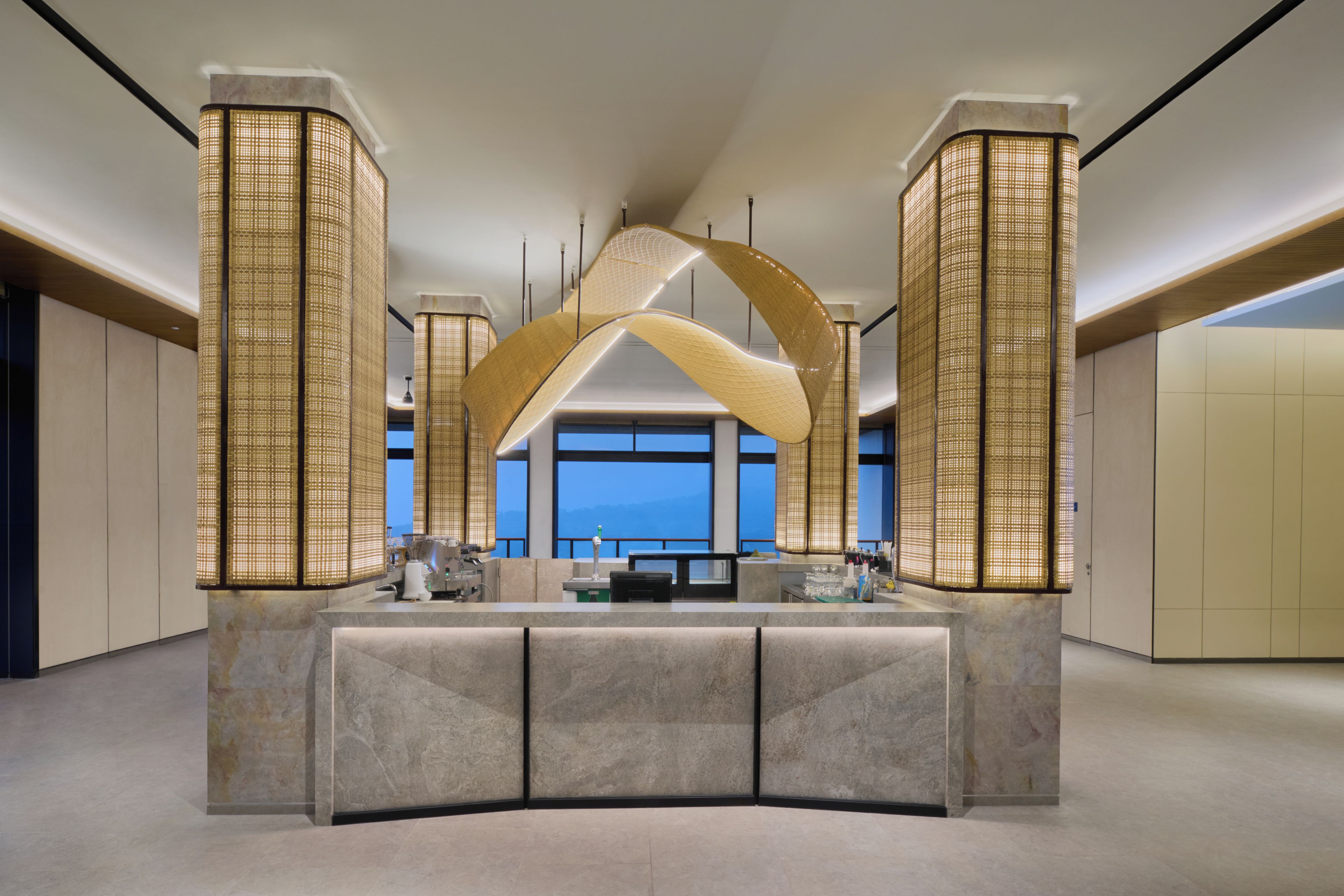 A modern hotel lobby with a central reception desk, large windows, and decorative lighting fixtures.