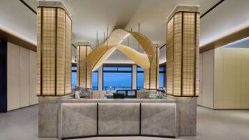 A modern hotel lobby with a central reception desk, large windows, and decorative lighting fixtures.