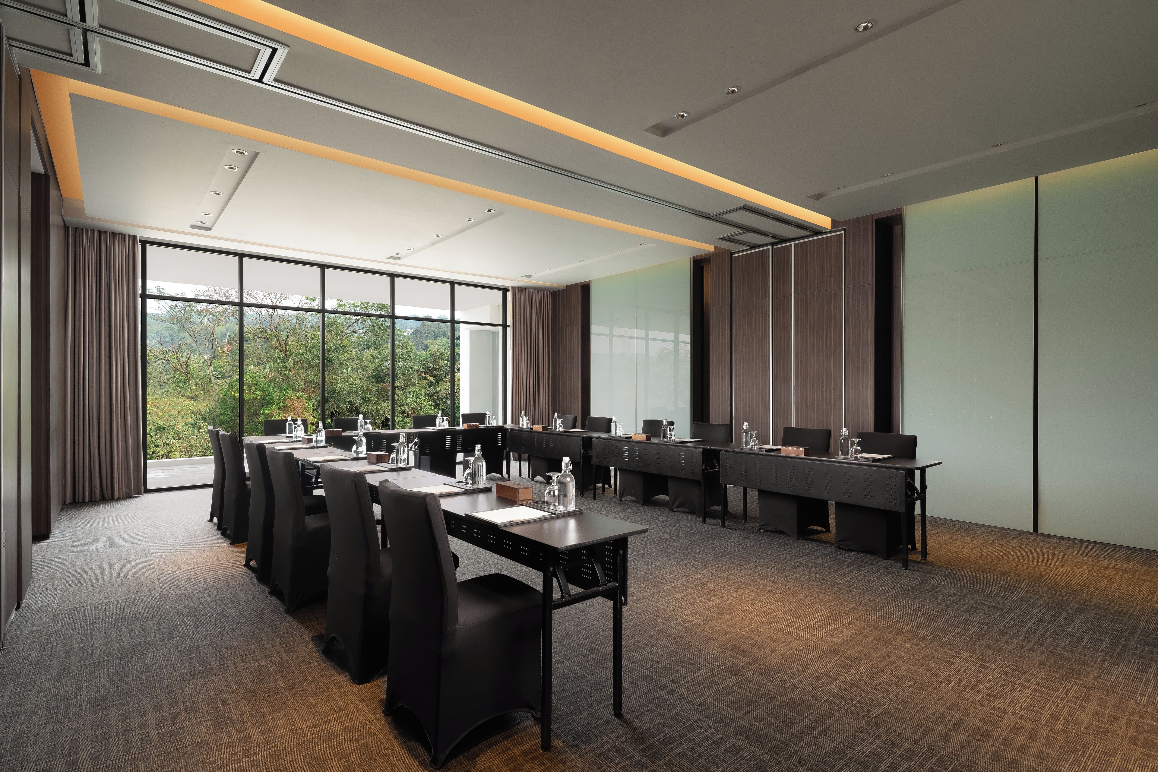 A conference room with a long table, chairs, and a view of greenery outside.