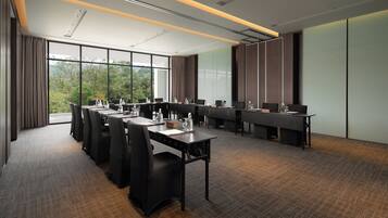A conference room with a long table, chairs, and a view of greenery outside.