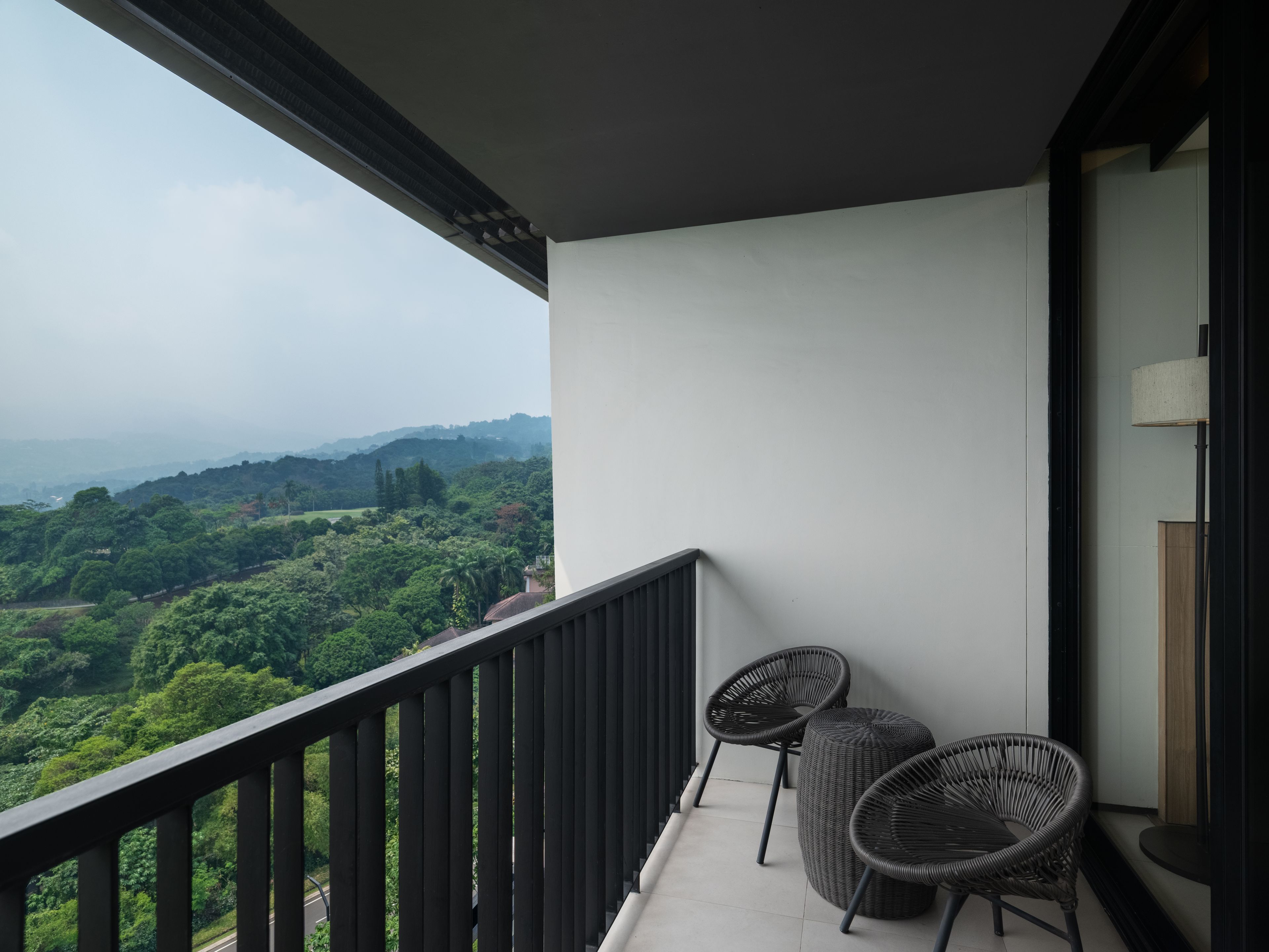 Ein Balkon mit Blick auf eine üppige Landschaft, zwei Korbstühle und ein kleiner Tisch.