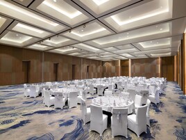 Un amplio salón de conferencias con varias mesas redondas, sillas blancas y una alfombra estampada.