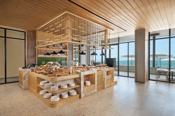 Una barra de desayuno moderna con diversas opciones de comida y vista al mar.