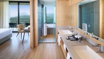 Ein modernes Hotelzimmer mit Balkon, einem großen Spiegel, einer Badewanne und einer separaten Sitzecke mit Sessel und Tisch.