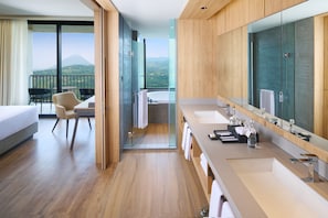 Habitación de hotel moderna con balcón, un espejo grande, bañera y un área de estar separada con una silla y una mesa.