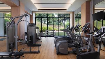 Un gimnasio moderno con diversos equipos de ejercicio, amplias ventanas y vista a zonas verdes.