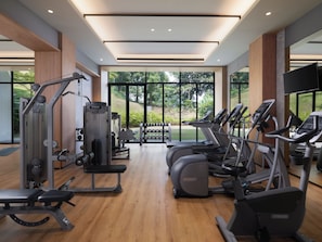 Un gimnasio moderno con diversos equipos de ejercicio, amplias ventanas y vista a zonas verdes.