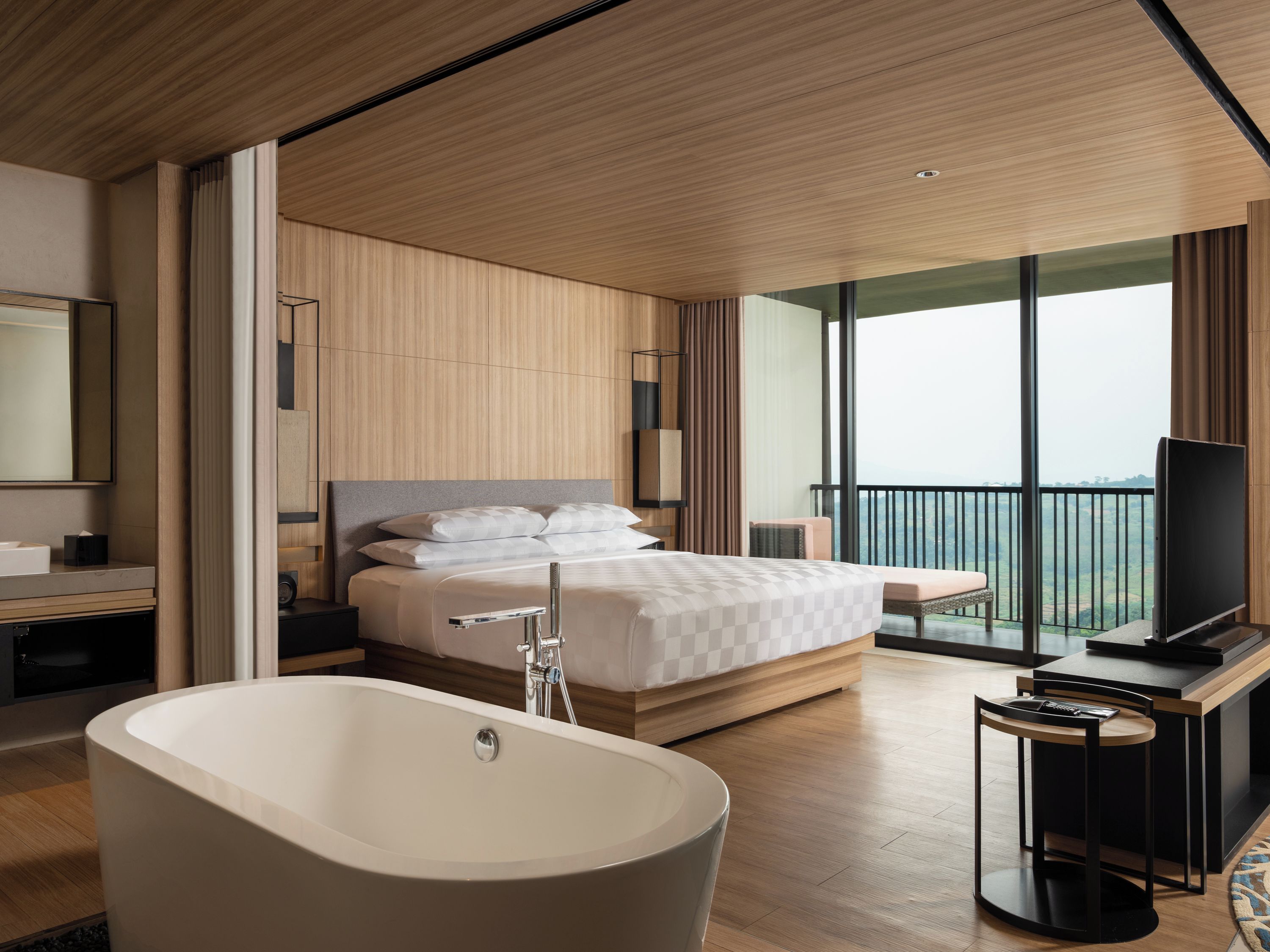 Habitación de hotel moderna con una cama grande, una bañera, un televisor y un balcón con vistas.