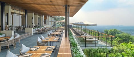 An outdoor dining area with wooden tables and chairs, a covered walkway, and a view of the landscape.