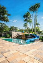 Una piscina con tobogán, rodeada de palmeras y un cielo despejado.
