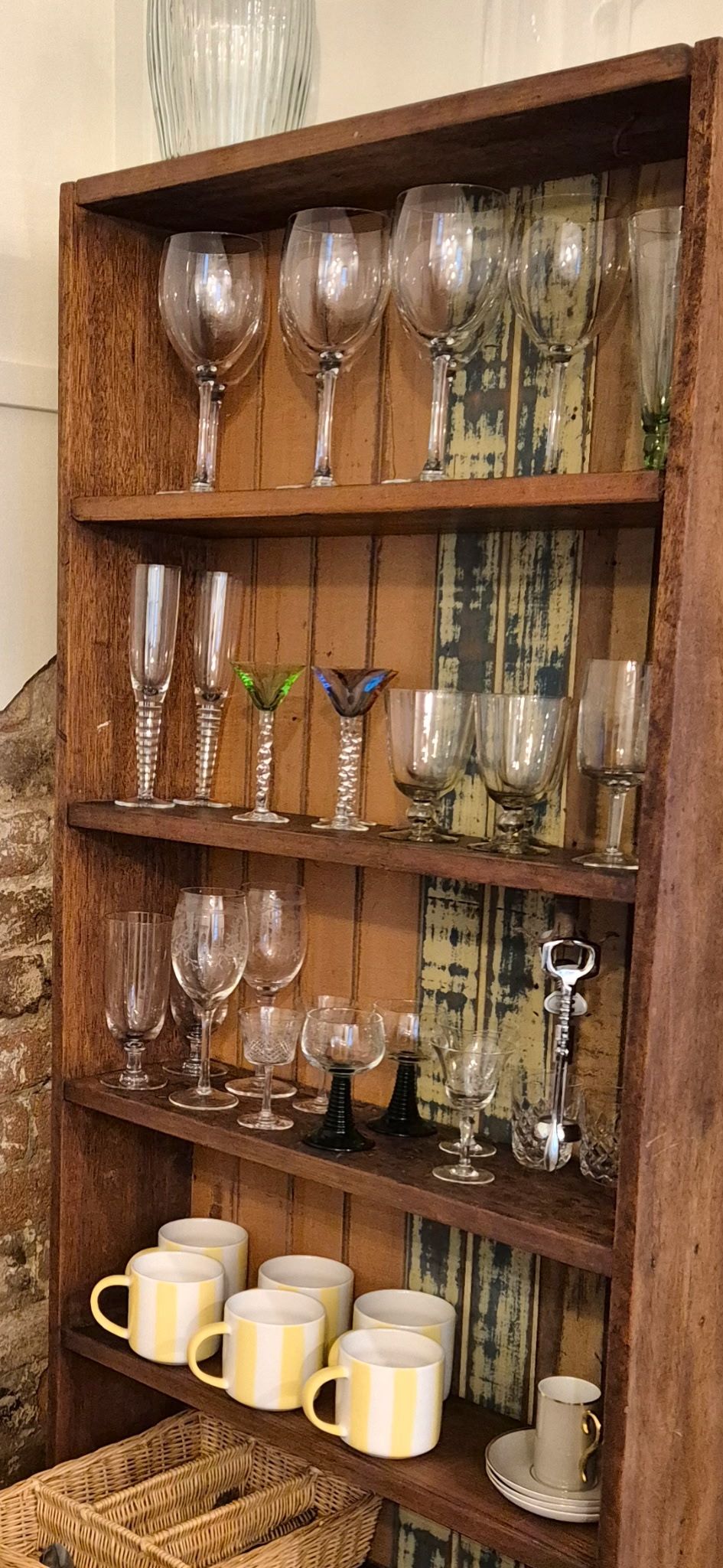 A wooden shelf with various glassware and mugs.
