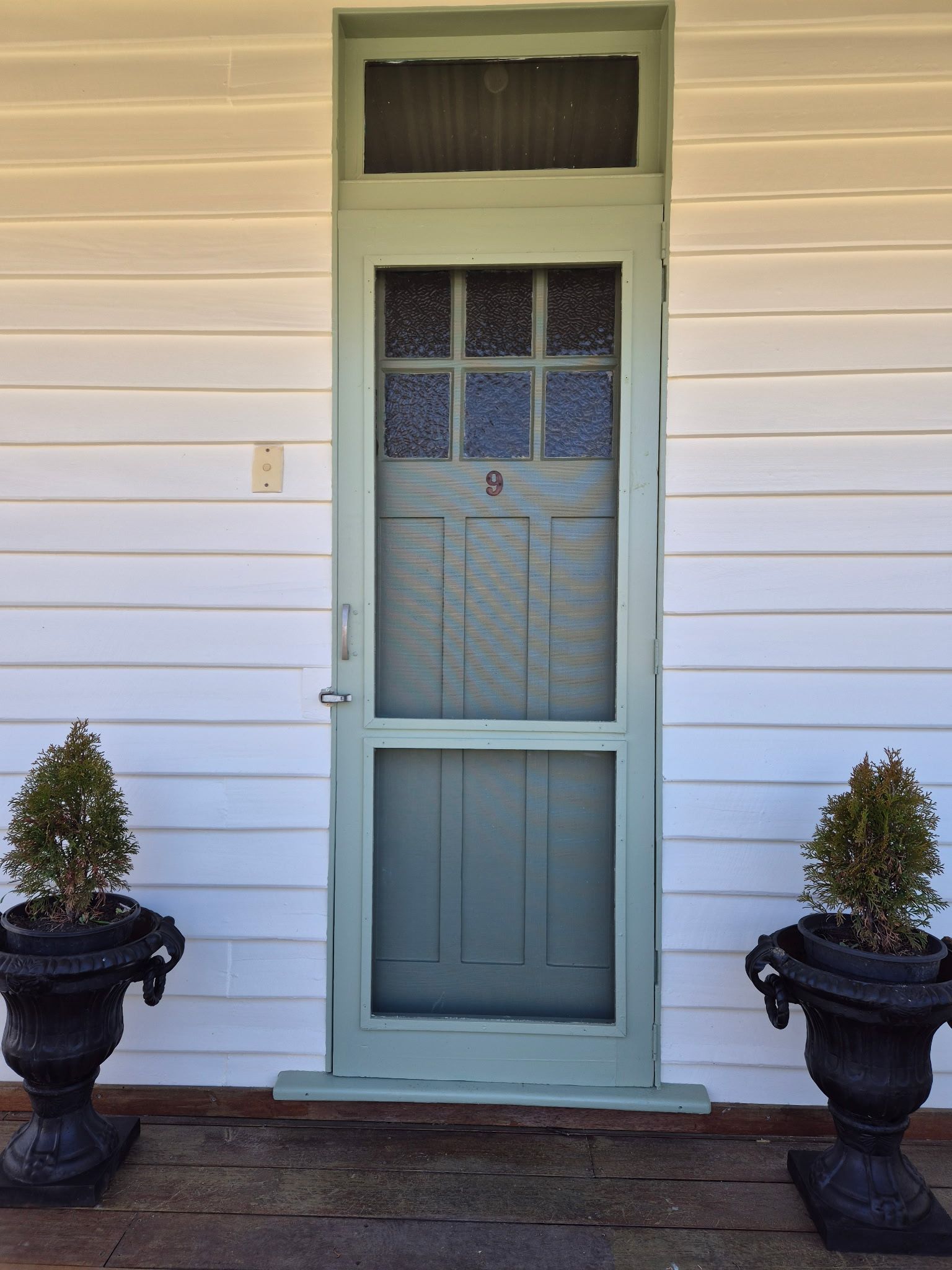 A front door with a number 9, flanked by two potted plants.