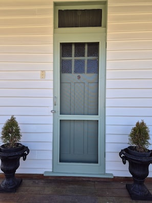 A front door with a number 9, flanked by two potted plants. - The Cottage on Malone (Braidwood)