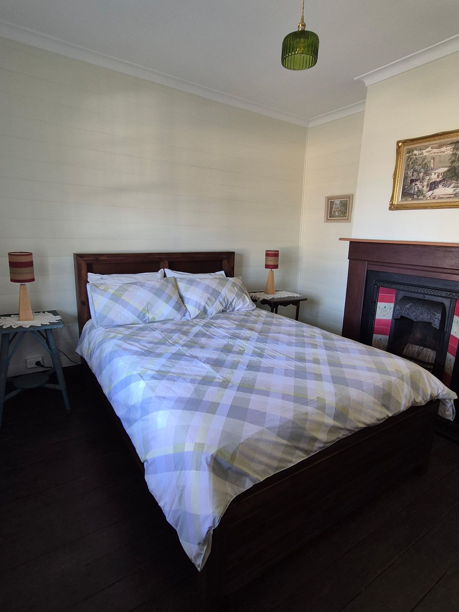 A neatly made bed with a checkered bedspread, two bedside tables with lamps, a fireplace, and a framed picture on the wall.