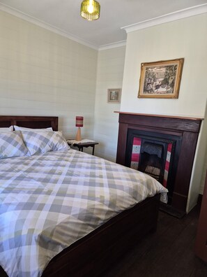 A bedroom with a bed, a fireplace, and a wall-mounted picture.