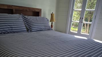 A bed with striped bedding, a wooden headboard, a bedside lamp, and a window with a view of trees.