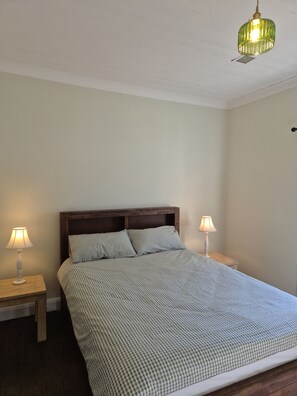 A bedroom with a bed, two bedside lamps, a wooden headboard, and a hanging light fixture.