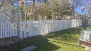 A white picket fence, a grassy yard, and a tree with pink blossoms.
