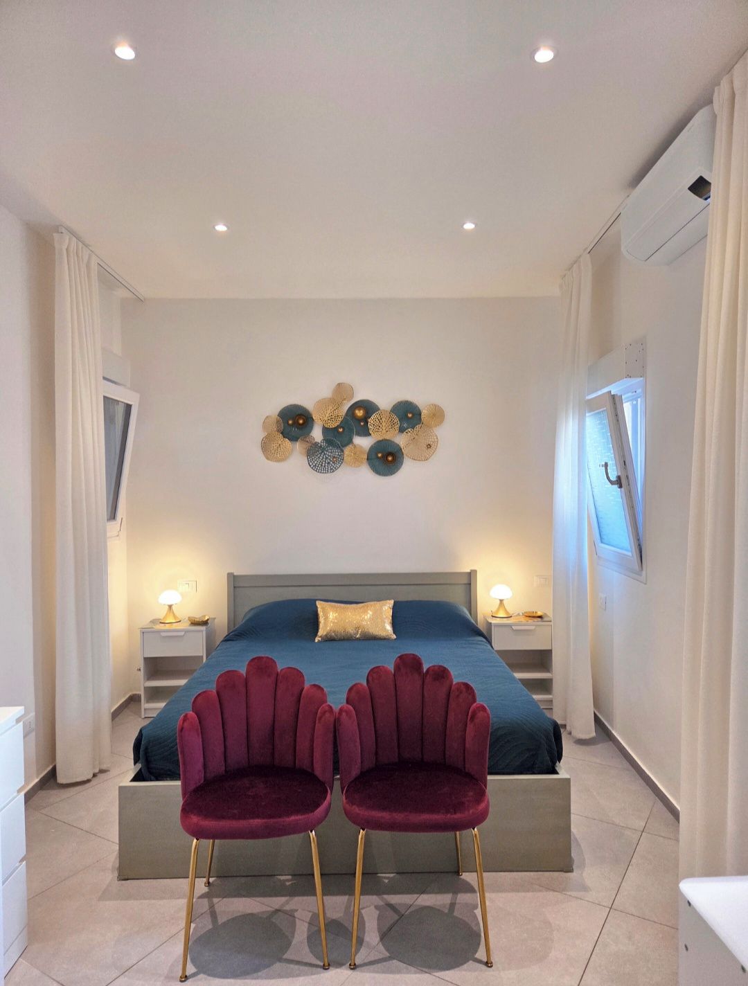 Een slaapkamer met een bed, twee nachtkastjes, een wanddecoratie en twee stoelen.