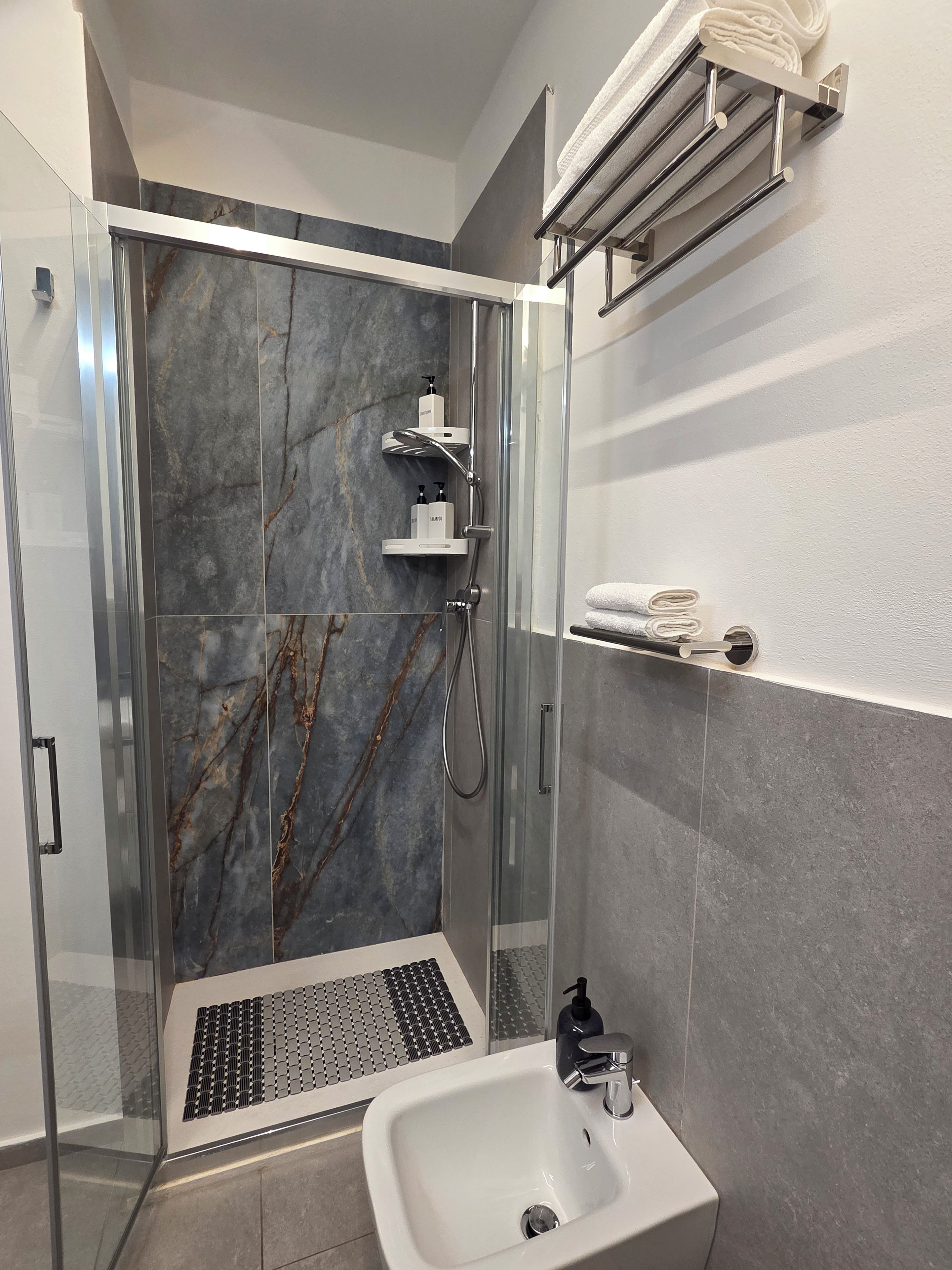 A modern bathroom with a glass-enclosed shower, a white sink, and a towel rack.