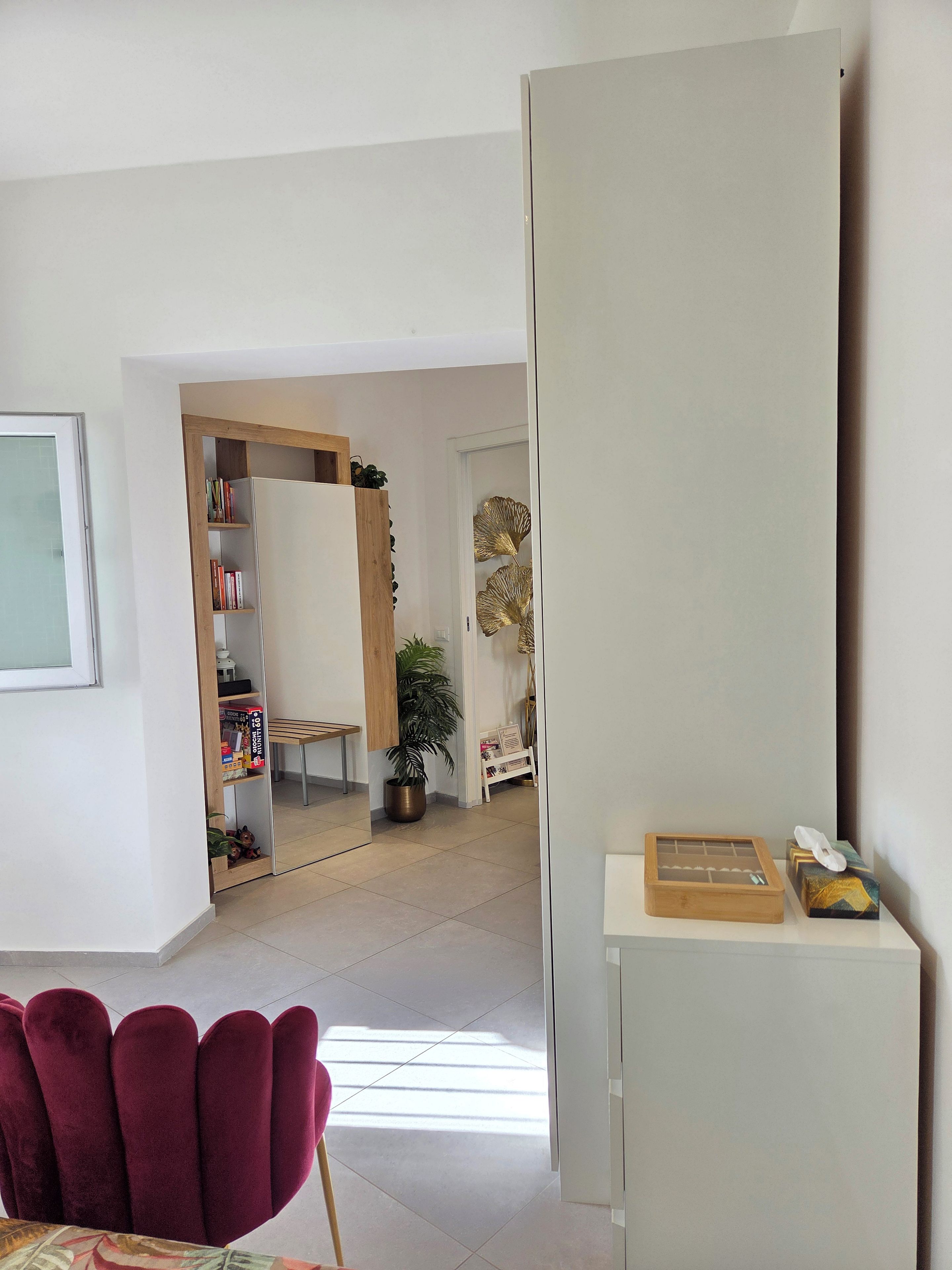 Un saló modern amb una cadira vermella, una biblioteca, un armari blanc i una planta en test.
