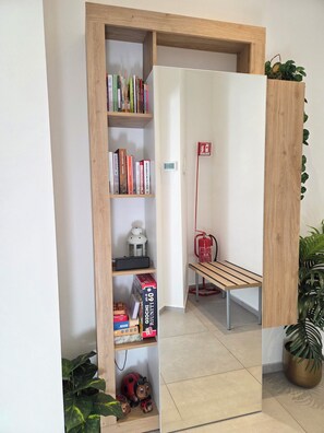 Quarto com estante de madeira, um banco, extintor de incêndio e planta em vaso.