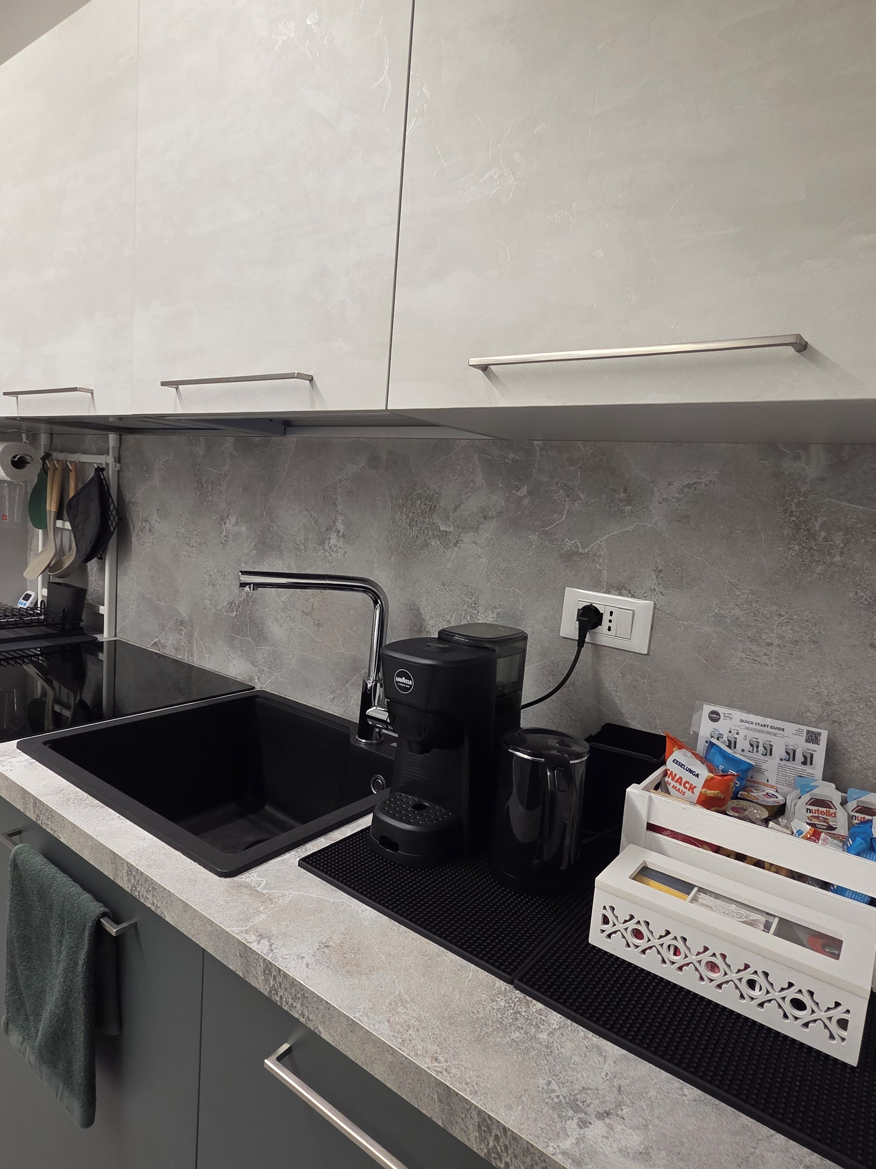 A modern kitchen with a black sink, a coffee maker, and a box of snacks.