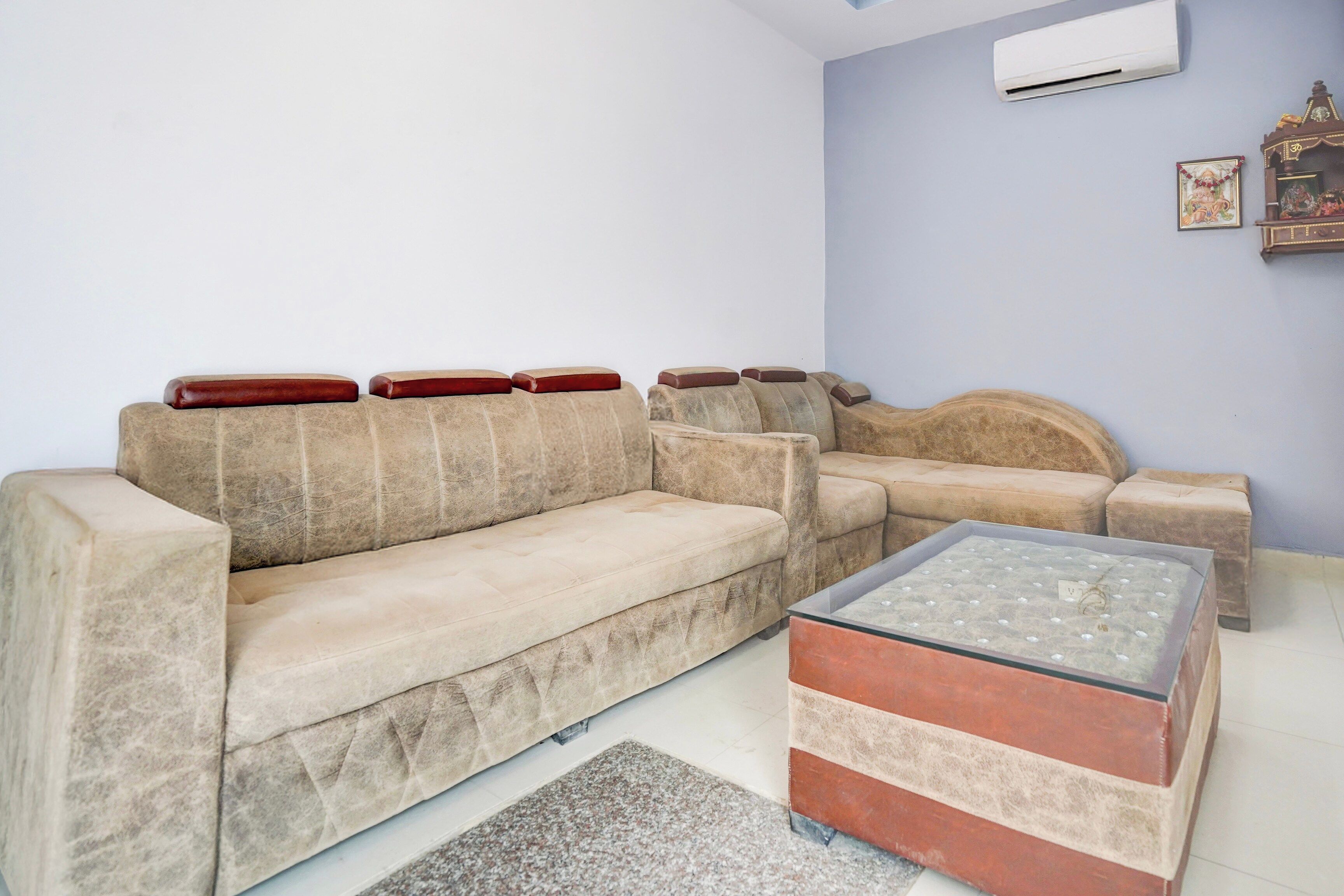 Una sala de estar con un sofá color beige, una mesa de centro de vidrio y una pequeña mesita de noche de madera.