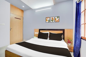 Une chambre d’hôtel avec un lit, une table de chevet, une lampe fixée au mur et une porte.