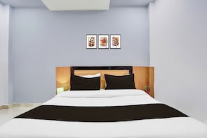 Une chambre d’hôtel avec un lit, une table de chevet, une lampe et trois tableaux encadrés accrochés au mur.