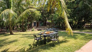 An outdoor dining area with tables and chairs, surrounded by lush greenery and palm trees. - Nagira Tranquility (Taveta)