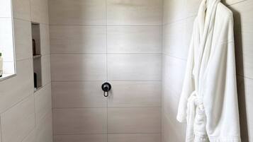 A modern shower stall with a handheld showerhead, a towel rack with a white towel, and a toilet in the corner.